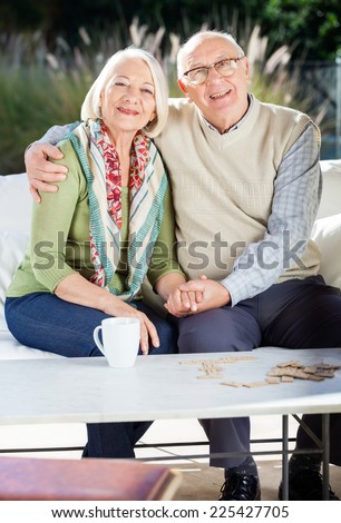 Portrait of happy senior couple sitting arm around on couch at nursing home porch