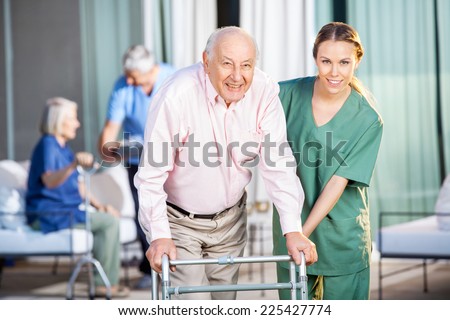 Portrait of happy female caretaker helping senior man in using Zimmer frame at nursing home yard