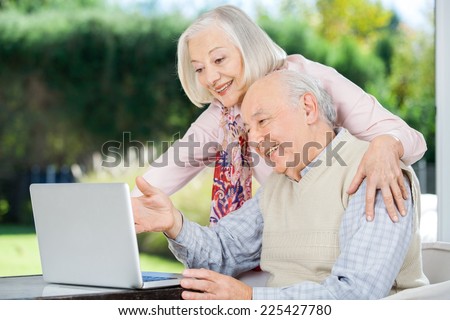 Cheerful senior couple using laptop at nursing home porch