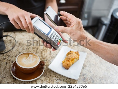 Cropped image of customer paying through mobilephone over electronic reader at cafe counter