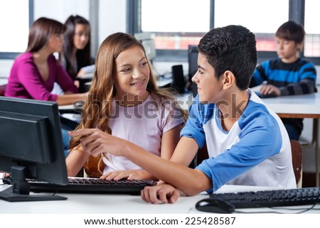 Teenage friends looking at each other while using computer in school lab