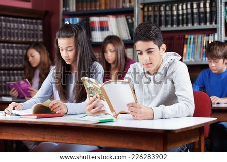 Male and female friends studying at table with classmates in library