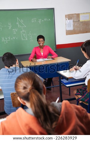 Portrait of young female teacher sitting with students in classroom