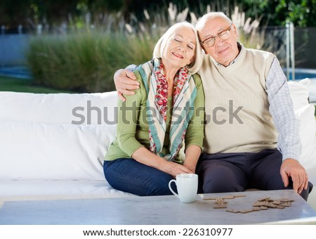 Relaxed senior man sitting with arm around woman on couch at nursing home porch