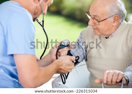 Male nurse checking blood pressure of senior man at nursing home