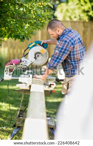Side view of mid adult manual worker cutting wood using table saw at construction site