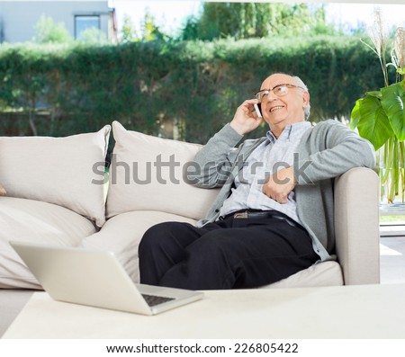 Relaxed senior man using mobile phone while sitting on couch at nursing home porch