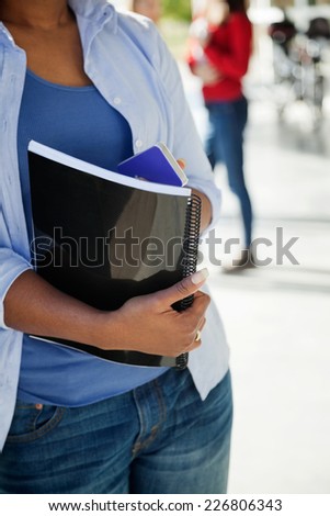 Midsection of female student with book and cellphone at university campus