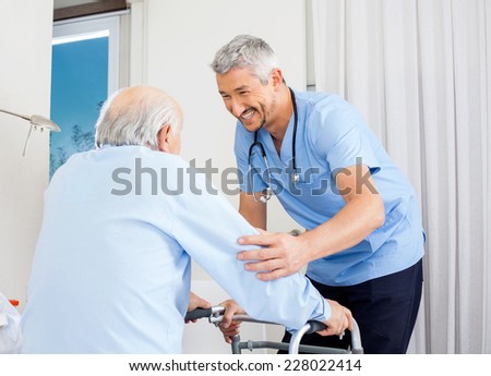 Smiling male caretaker helping senior man to use walking frame in bedroom at nursing home