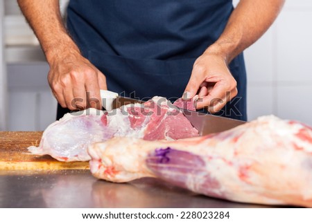 Midsection of male butcher cutting raw meat with knife at counter in shop