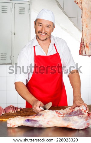 Portrait of confident mature male butcher cutting meat at counter in butchery