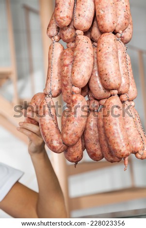 Cropped image of female butcher holding sausages hanging in butchery