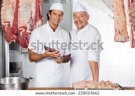 Portrait of happy butchers with digital tablet at counter in butchery