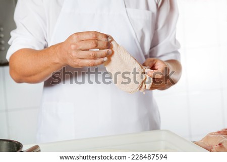 Midsection of mature butcher holding chicken meat covered with flour in shop