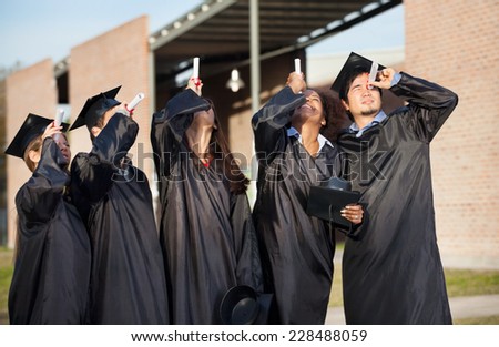 Multiethnic university students in graduation gown looking through certificates on campus