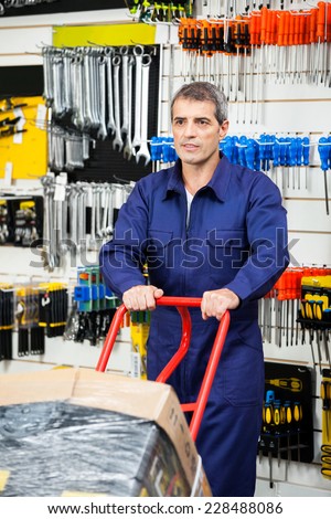 Mature worker in overalls pushing trolley in hardware shop