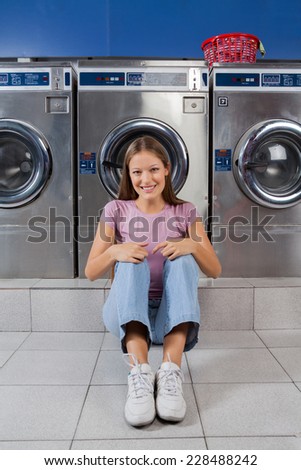 Portrait of beautiful young woman sitting on floor against washing machines at laundry