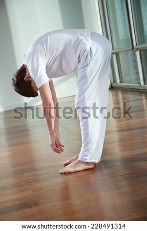 Full length of a young man practicing yoga called Standing Forward Bend at gym