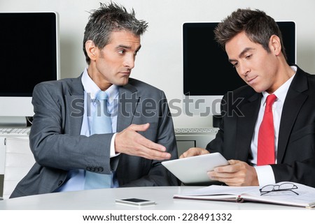 Young businessman using digital tablet while sitting with colleague at desk in office