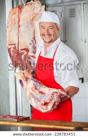 Portrait of happy mature male butcher carrying meat at counter in butchery