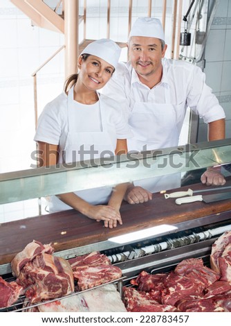Portrait of friendly butchers standing at meat counter in butchery