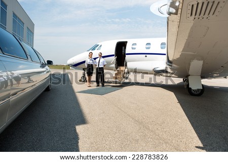 Stewardess and pilot standing neat limousine and private jet at airport terminal