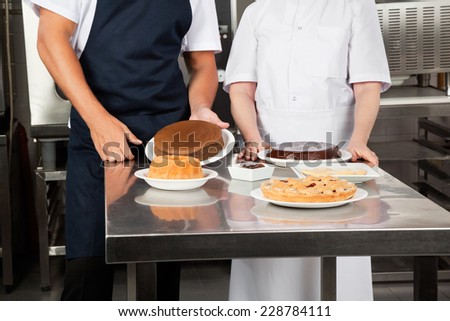 Midsection of chefs with sweet dishes at commercial kitchen counter