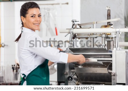 Portrait of happy female chef processing ravioli pasta in machine at commercial kitchen