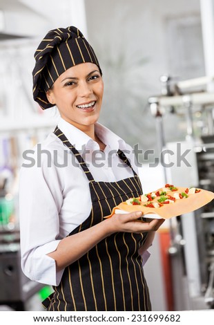 Portrait of happy chef holding tray with stuffed ravioli pasta sheet in commercial kitchen