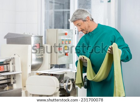 Male chef looking at machine while holding green spaghetti pasta sheet at commercial kitchen