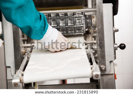 Cropped image of male chef\'s hand removing ravioli pasta from machine at commercial kitchen