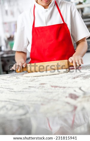 Midsection of chef rolling dough at messy counter in commercial kitchen