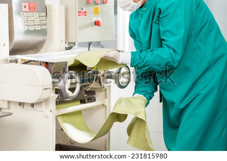 Midsection of male chef in protective workwear processing spaghetti pasta sheet in machine at commercial kitchen