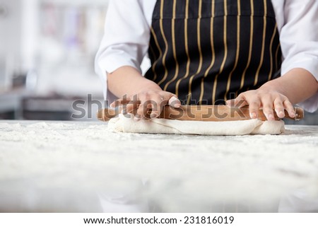 Midsection of female chef rolling dough at messy counter in commercial kitchen