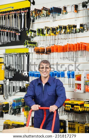 Mature worker in overalls pushing trolley while looking away in hardware shop