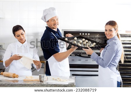 Portrait of smiling female chef passing baking sheet to male colleague by oven in commercial kitchen