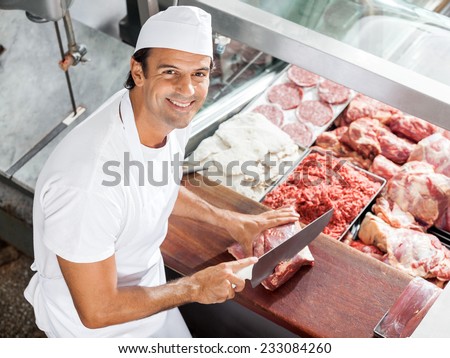 High angle portrait of smiling butcher cutting meat at counter in butchery
