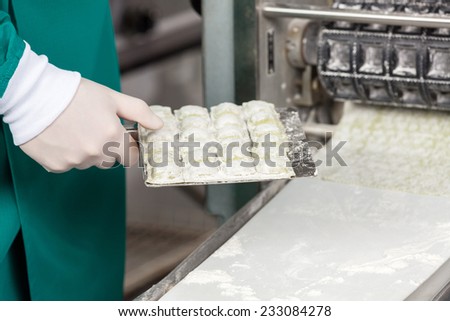 Midsection of male chef holding ravioli pasta tray by automated machine at commercial kitchen