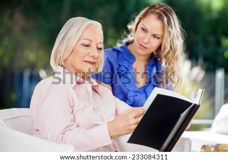 Granddaughter looking at grandmother reading book on nursing home porch