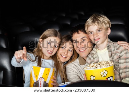 Happy girl showing something to family while watching movie in cinema theater