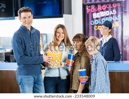 Portrait of happy family of four holding snacks while female worker standing at cinema concession stand