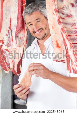 Portrait of confident mature butcher holding chicken meat in shop