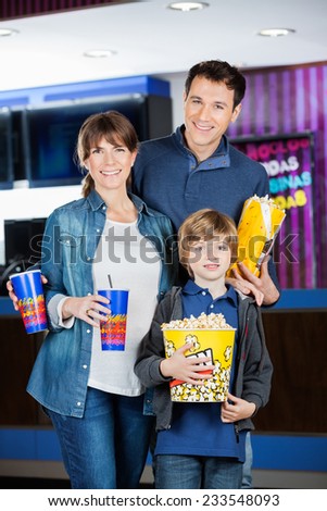 Portrait of happy family holding popcorns and drinks at cinema
