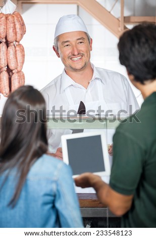 Happy mature butcher with couple using digital tablet at butchery counter