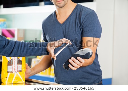 Cropped image of man placing smartphone over credit card reader to make payment at cinema concession stand