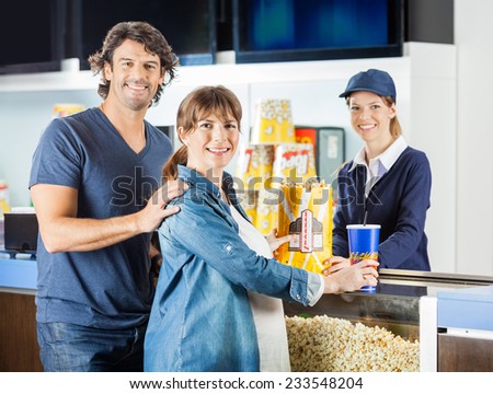 Portrait of expectant couple buying popcorn and drink from female seller at cinema concession stand