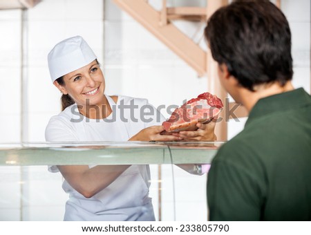 Happy mature female butcher selling fresh meat to male customer at store