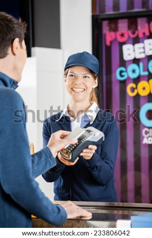 Happy female worker taking payment from man through NFC technology at cinema concession stand