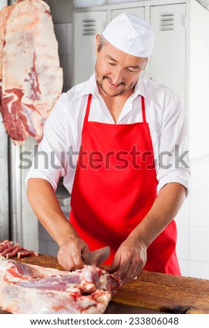 Mature male butcher cutting fresh meat at counter in butchery
