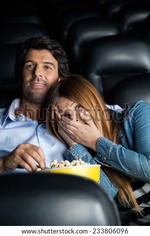 Scared mid adult woman leaning on man while watching movie in cinema theater